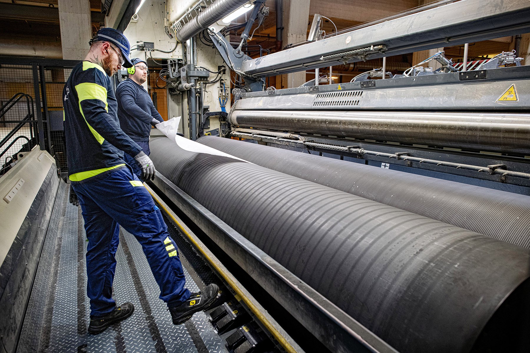 Elämää helpottava työaikamuoto. Jälkikäsittelijä Iiro Vilkas ei voisi kuvitella tekevänsä muuta kuin 12-tuntista vuoro­järjestelmää.
Taneli Miettinen vie rullan päätä leikkurin telojen väliin
Pituusleikkurinhoitaja Sebastian Pesola ja Taneli Miettinen vetävät päätä leikkurille.
 Iiro Vilkas siirtää tampuurin leikkurille. 